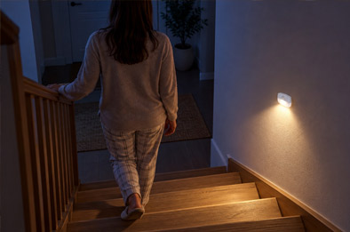 Veilleuse LED blanche collée au mur d'un escalier qui s'allume automatiquement au passage d'une personne la nuit, halo blanc chaud sur les marches