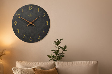 Horloge murale en bois noir de 30 cm avec chiffres dorés installée au-dessus d’un canapé beige