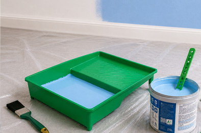 Bac à peinture vert rempli de peinture bleue, avec pinceau, rouleau et bâtonnet mélangeur