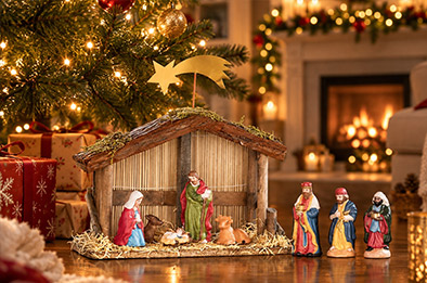 Crèche de Noël en bois avec figurines en porcelaine installée au pied d'un sapin illuminé, cheminée décorée en arrière-plan