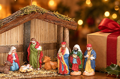 Crèche de Noël en bois posée sur une table avec un paquet cadeau au ruban rouge et du houx