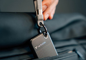 Disque dur SSD Verbatim noir accroché à un sac à dos grâce à une dragonne grise. Pratique pour le transport.