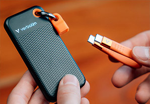 Disque SSD externe Verbatim avec dragonne orange posé sur une table en bois