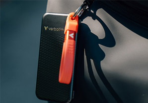 SSD Verbatim noir avec dragonne rouge fixé à un sac, idéal pour un transport nomade.