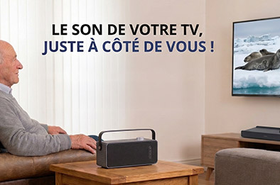 Personne âgée assise dans un salon regardant la télévision avec un haut-parleur TV sans fil posé sur la table à côté